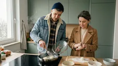 Para w kuchni: mężczyzna wkłada na patelnię kulki syrników, kobieta formuje ciasto