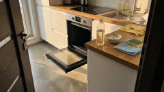 Otwarty piekarnik elektryczny w kuchni, na blacie butelka octu, ściereczki i gąbka